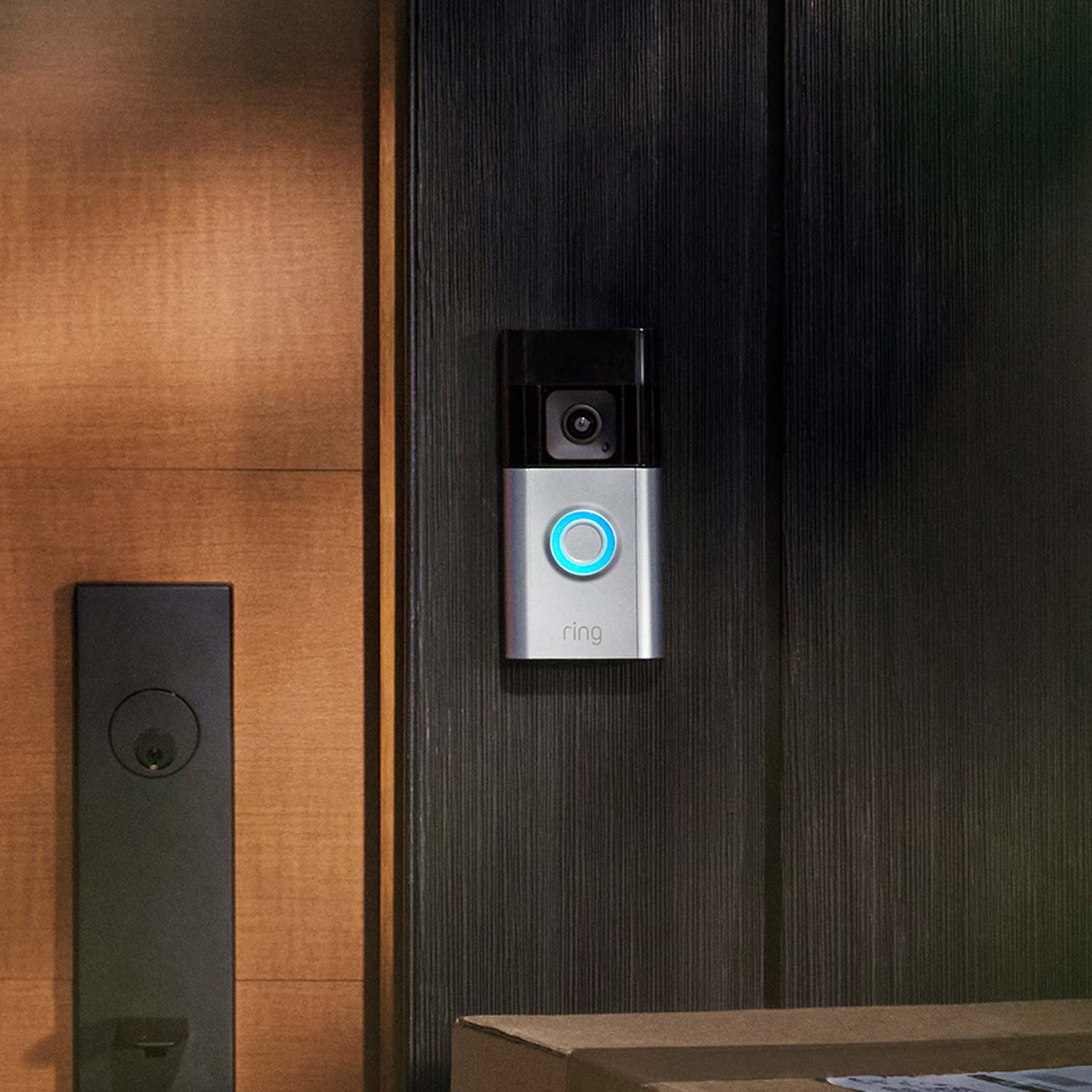 Battery Doorbell Pro - Ring Battery Doorbell Pro with blue-lit button mounted next to door, with door hardware visible and package on doorstep.