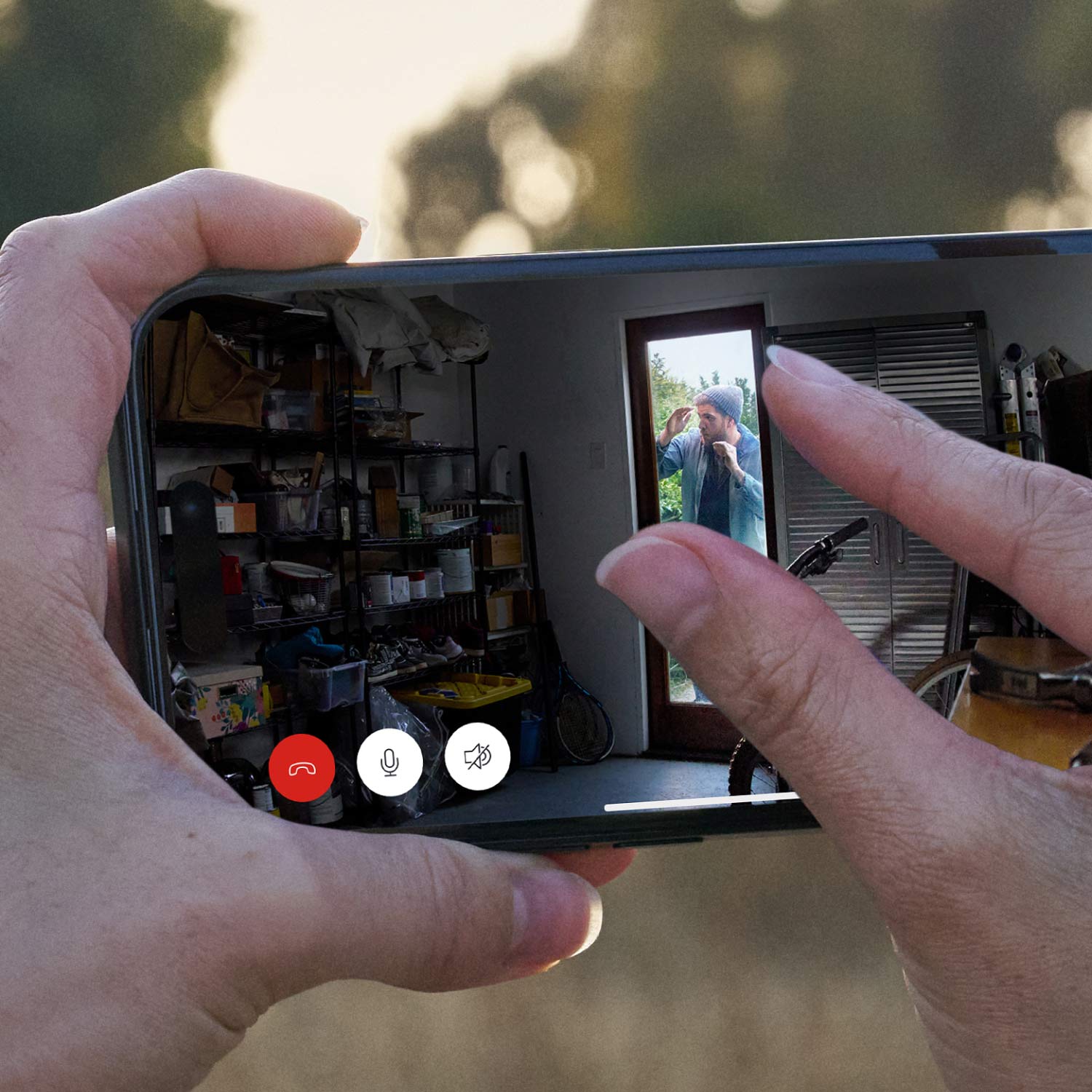Indoor Cam Plus (Featuring Retinal 2K) - Hands holding a horizontal phone with  fingers pinching in to zoom. Screen shows a stranger peering through the glass of a garage door.
