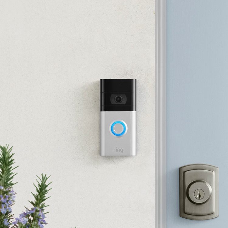 Ring Video Doorbell with blue-lit button on a white wall beside light-blue door equipped with deadbolt lock.
