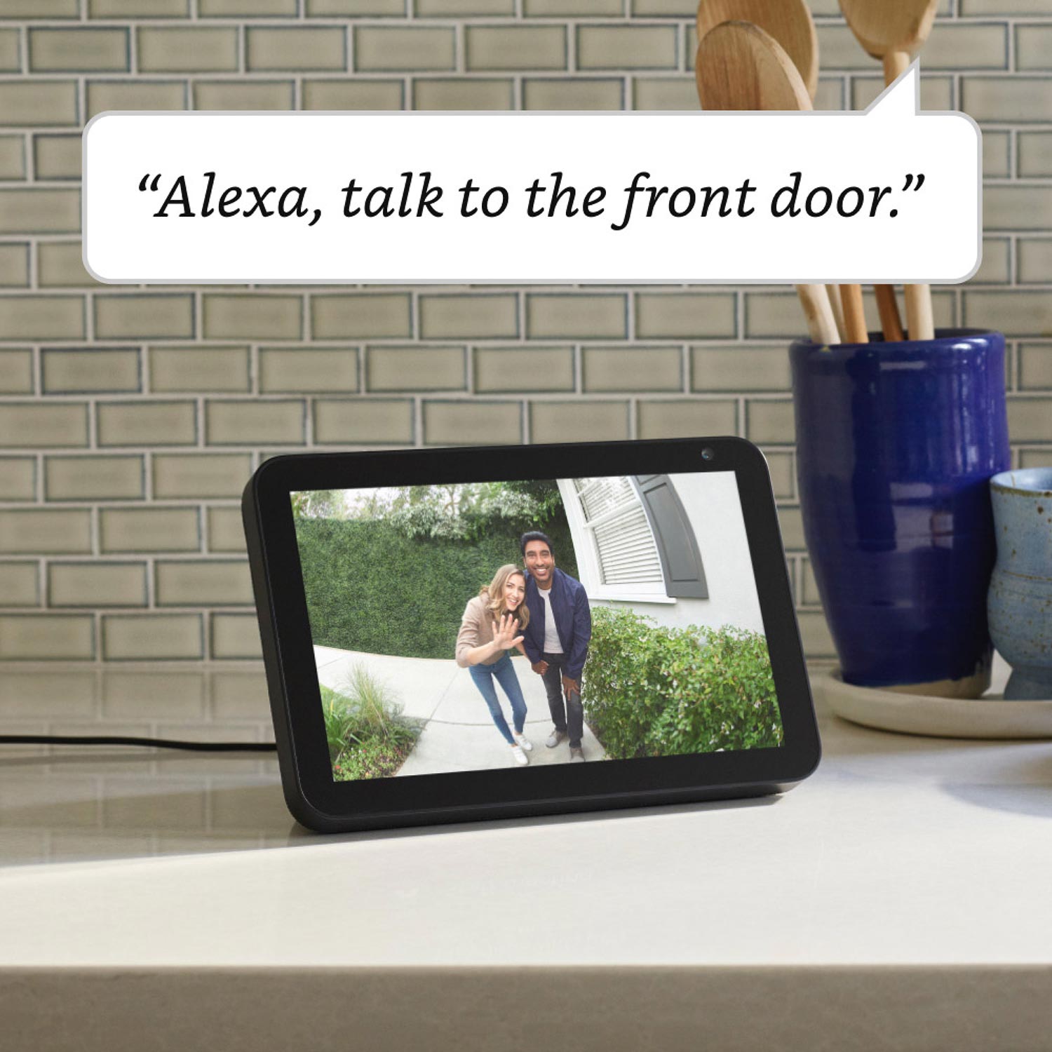 Video Doorbell Wired - Smart display on kitchen counter shows live video of two visitors at front door with Alexa command overlay.