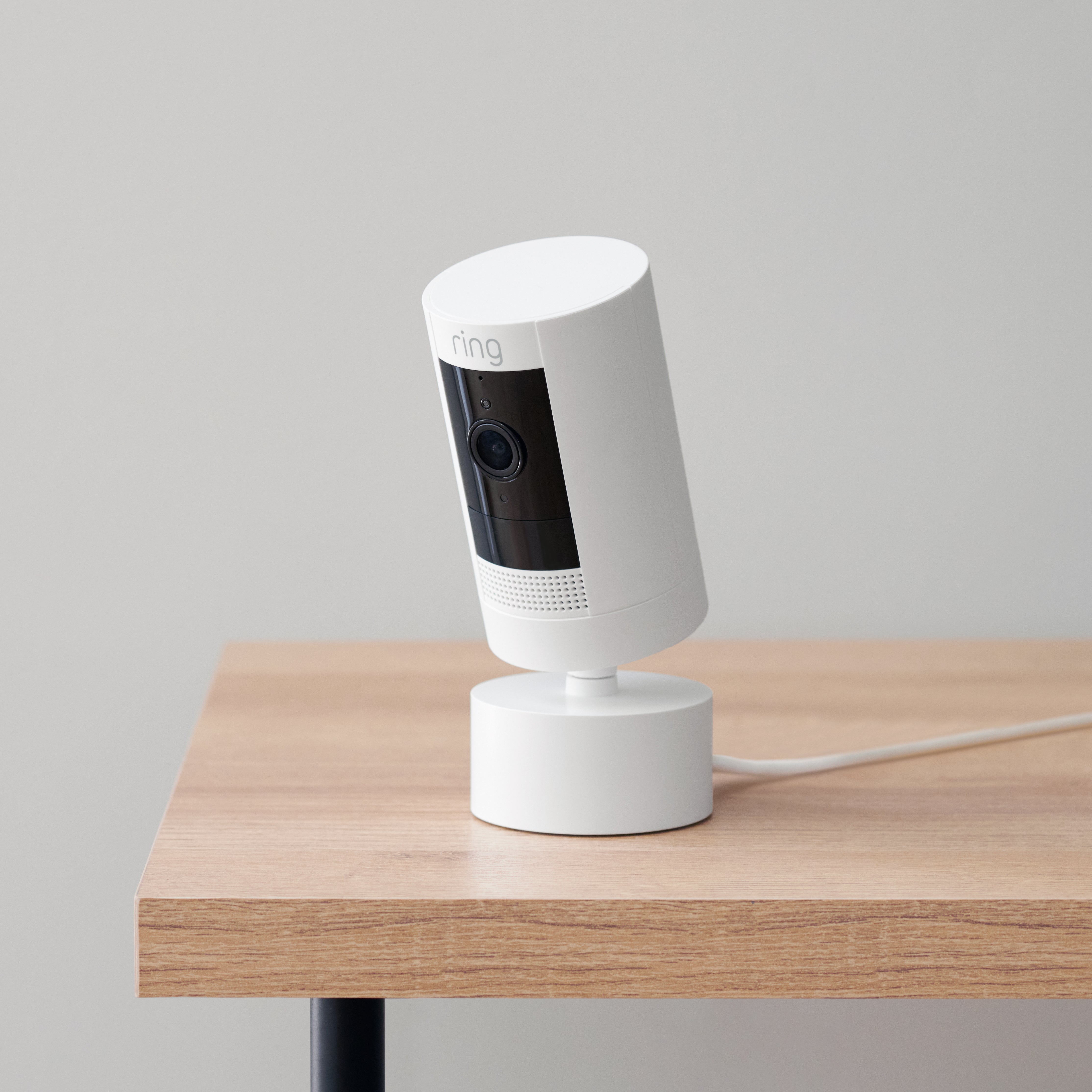 Pan-Tilt Mount with Indoor/Outdoor Power Adapter (for Stick Up Cam Plug-In, 3rd Gen) - White Ring Stick Up Cam with power cable, attached to a Pan-Tilt Mount with Indoor/Outdoor Power Adapter, on table.