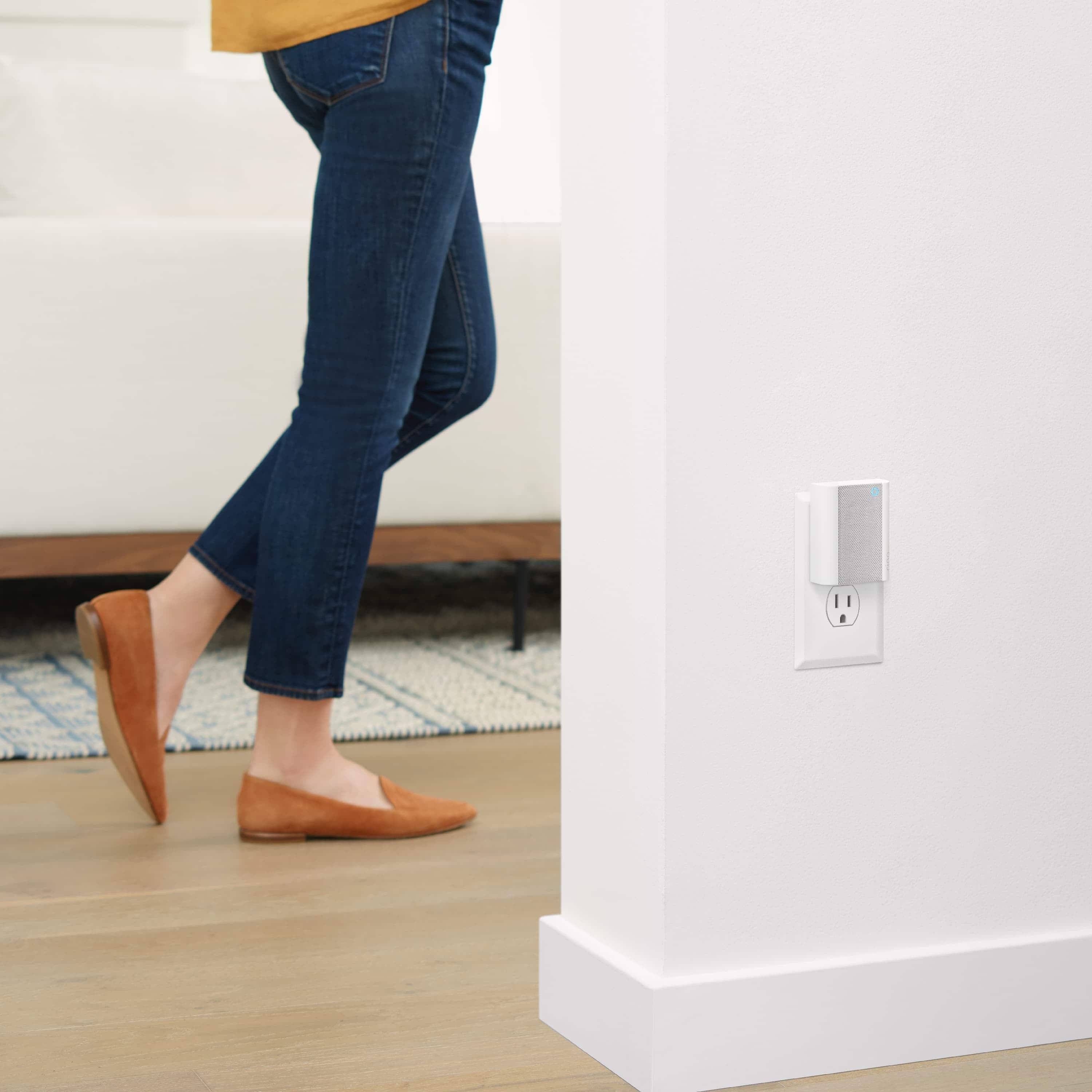 Chime - Chime: Ring Chime plugged into wall outlet with a woman wearing bluejeans walking by in the background.