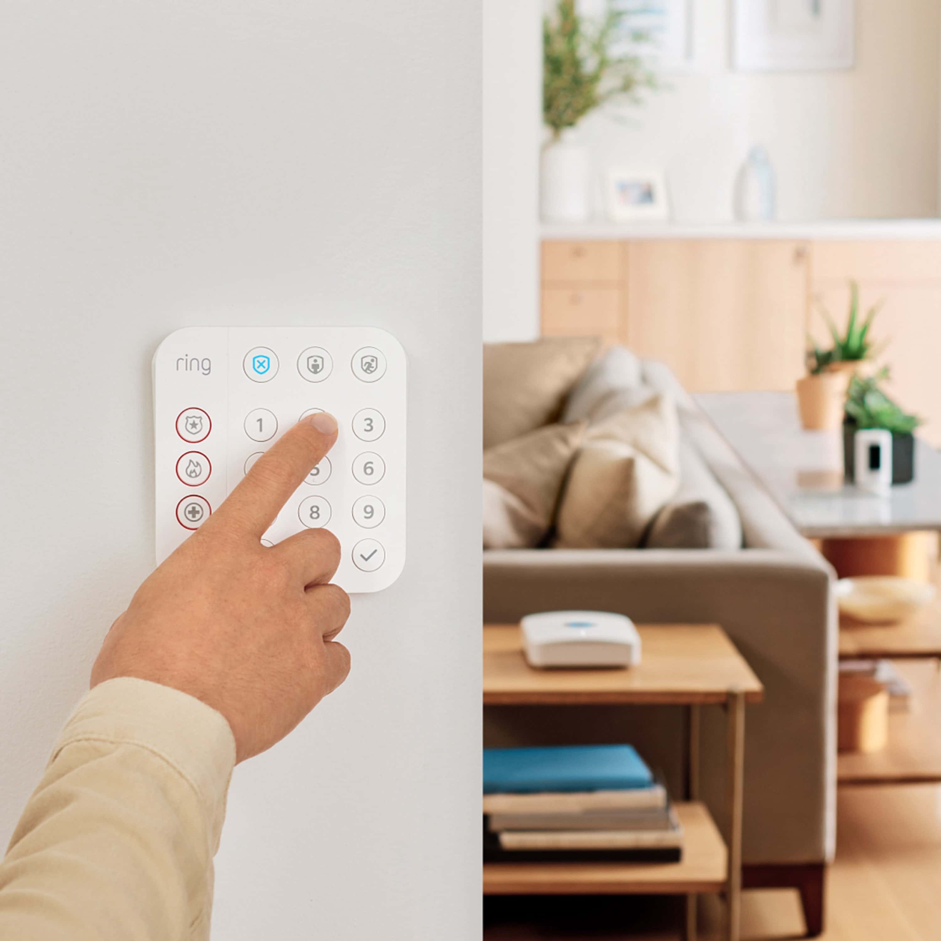 Protected Basic Kit (Battery Doorbell + Alarm 5-Piece Security Kit) - Person pressing button on white Ring Alarm Keypad on wall, with a living room and Ring Base Station in the background.