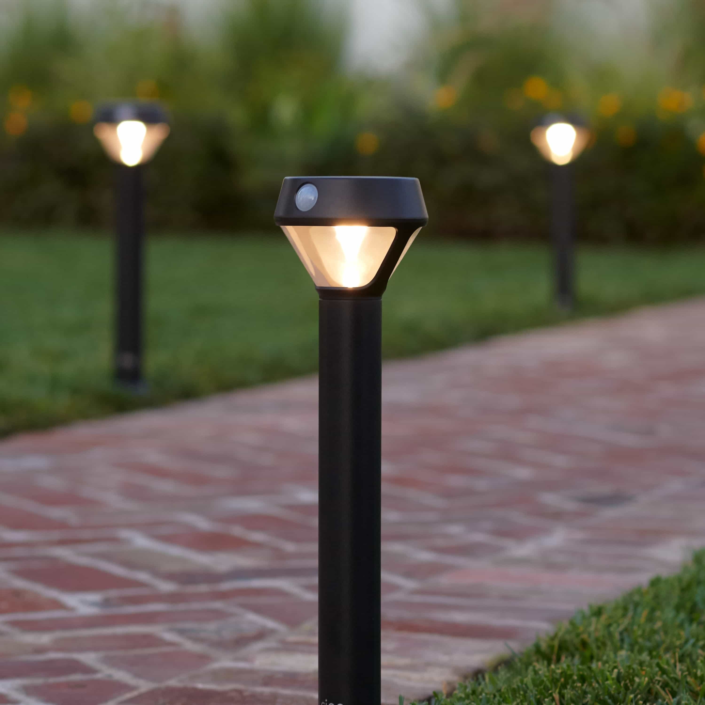 Smart Lighting Solar Pathlight - Ring Solar Pathlights line a brick walkway, glowing softly at dusk to light paths when motion is detected.