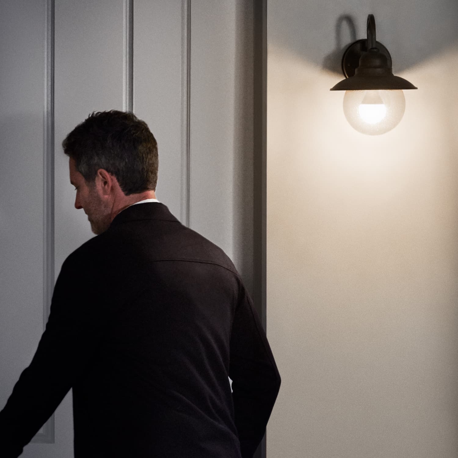 Smart Lighting A19 Smart LED Bulb - Man unlocking a door at night under wall-mounted outdoor porch light illuminated by an A19 Smart LED Bulb.