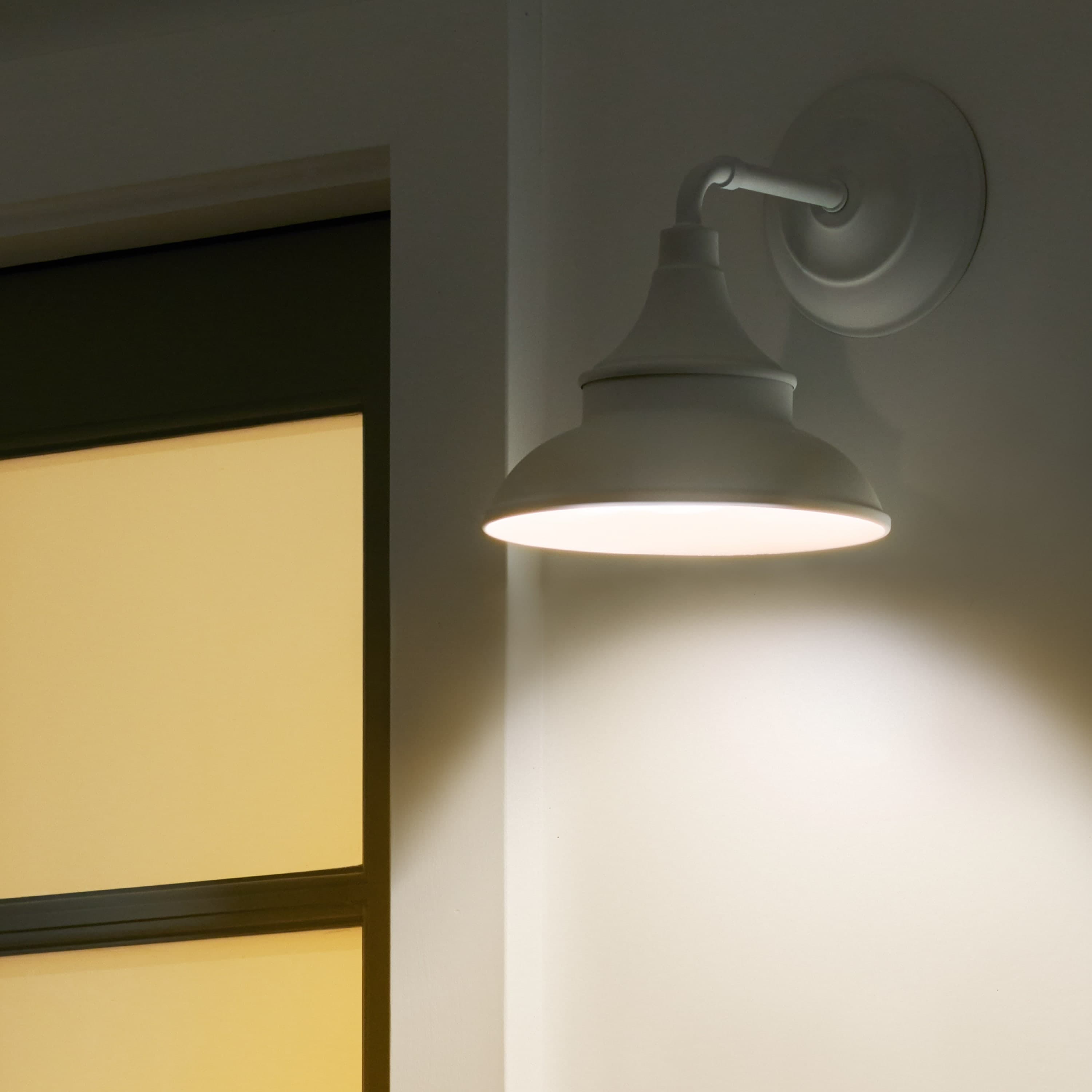 Smart Lighting A19 Smart LED Bulb - A19 SMart LED Bulb glowing inside a white outdoor wall sconce, casting light on a white wall near a window.