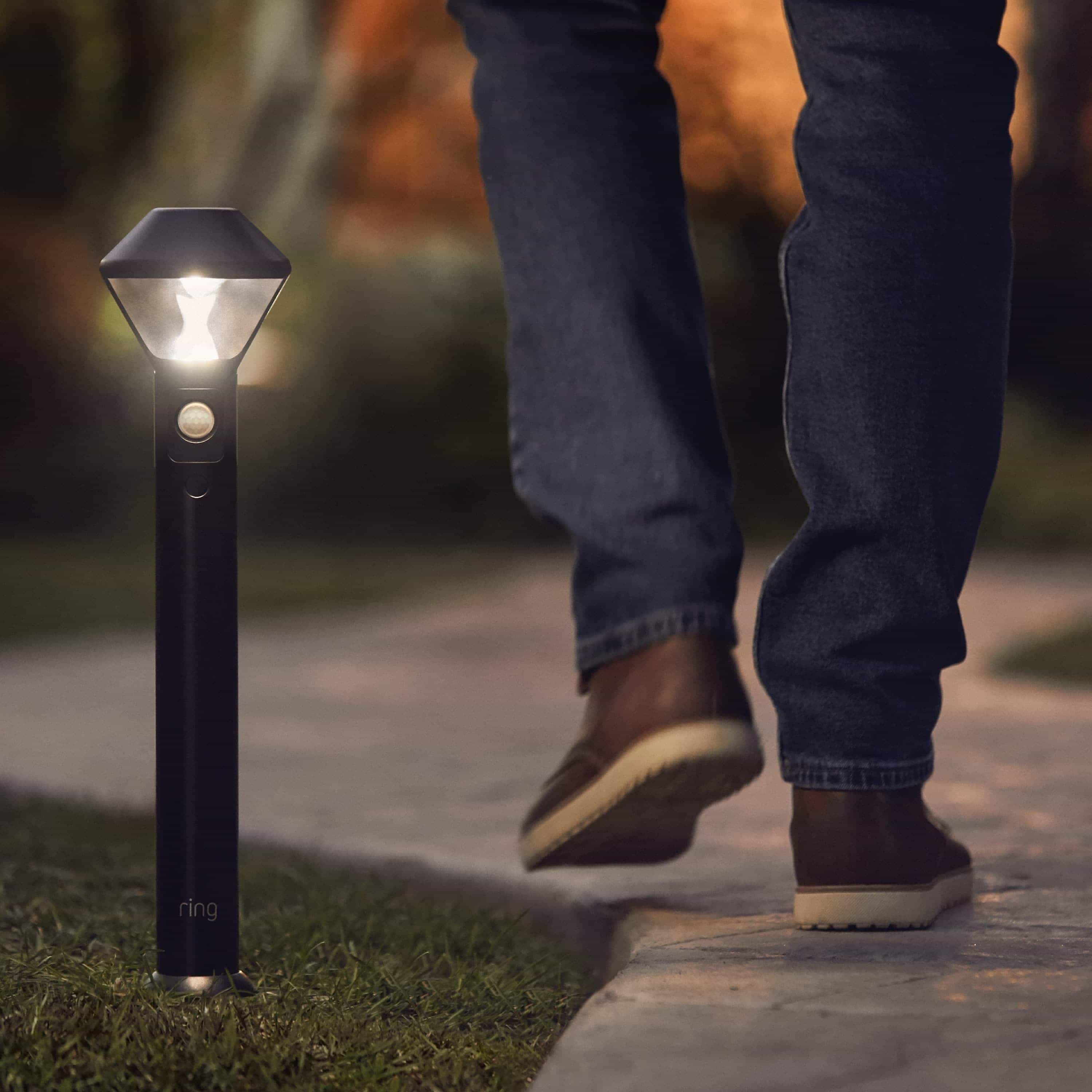 Smart Lighting Pathlight Battery - Person walking on a path at night, illuminated by a motion-activated Ring Smart Lighting Pathlight.