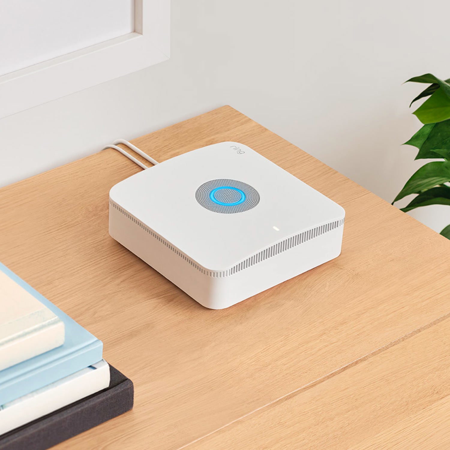 Alarm Pro Base Station (for with built-in eero Wi-Fi 6 router) - White Ring Alarm Pro Base Station with glowing blue light ring, sitting on a wooden table near books and a plant.