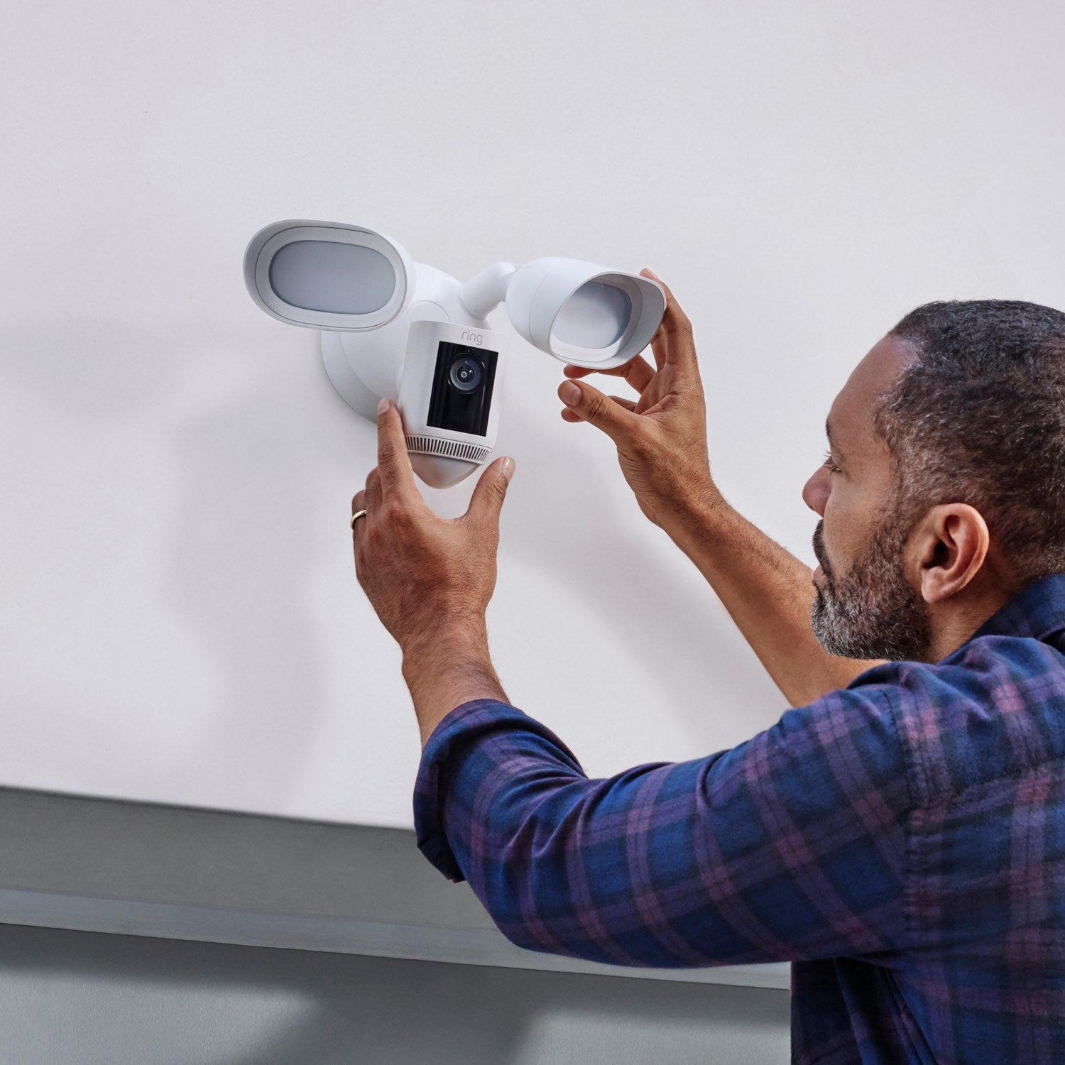 Floodlight Cam Pro (Certified Refurbished)     - Man wearing adjusting a white Ring Floodlight Cam Pro mounted on an exterior wall.