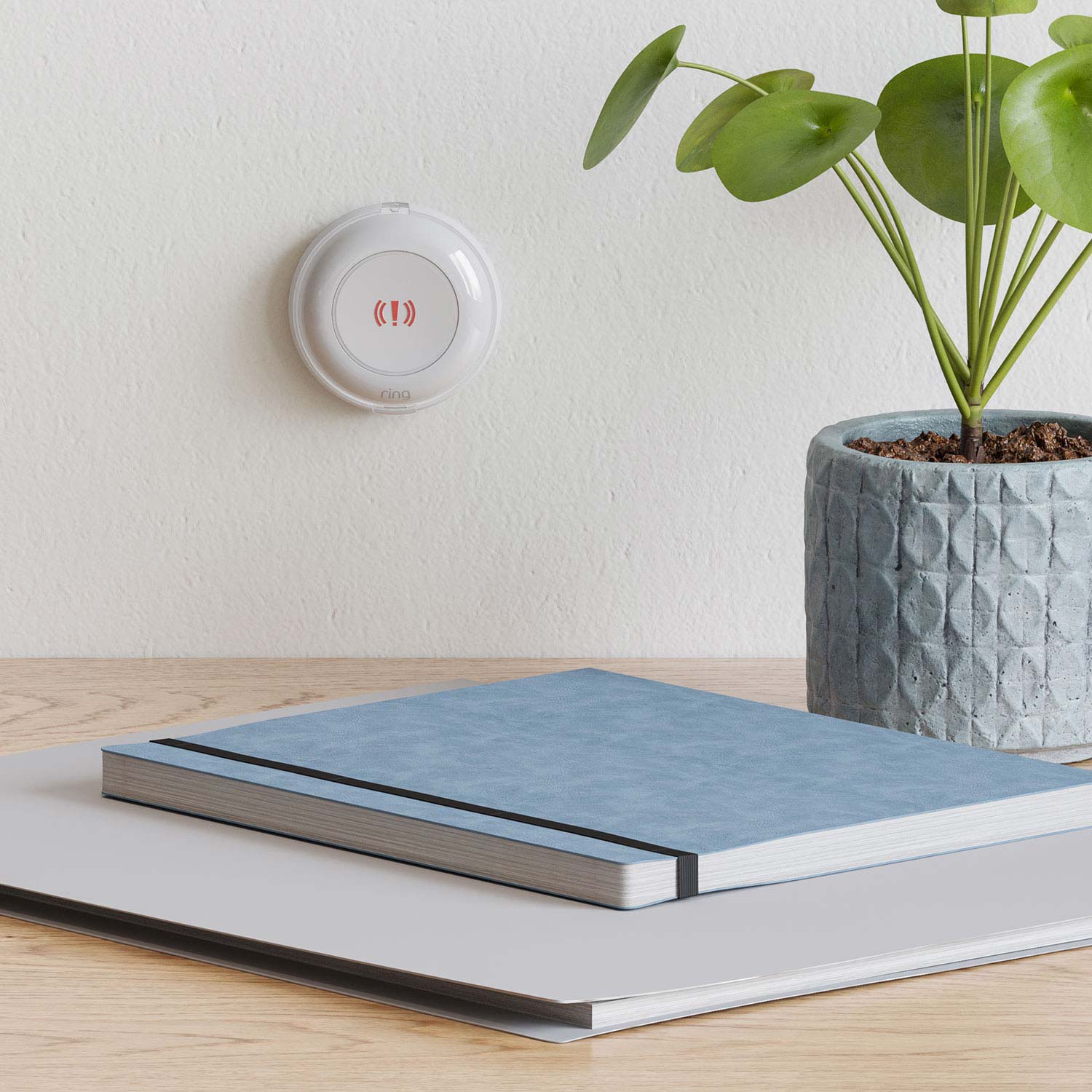2-Pack Panic Button (2nd Gen) - Ring Panic Button mounted on a wall above a desk with a plant and notebooks, ready to trigger an alarm in an emergency.