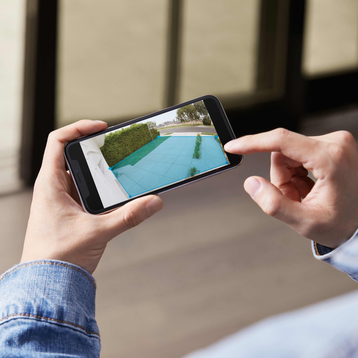 Floodlight Cam Wired Plus (Certified Refurbished) - Person viewing outdoor security camera footage, adjusting Ring Floodlight Cam Wired Plus setting using Ring App.