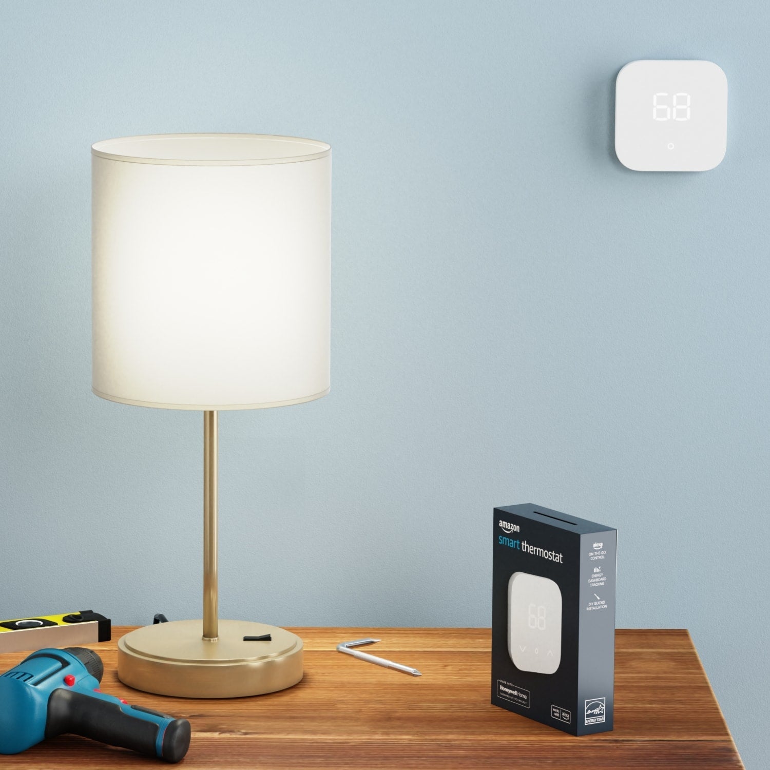Amazon Smart Thermostat - Amazon Smart Thermostat mounted on a wall above a table with lamp, drill, tools, and product box.