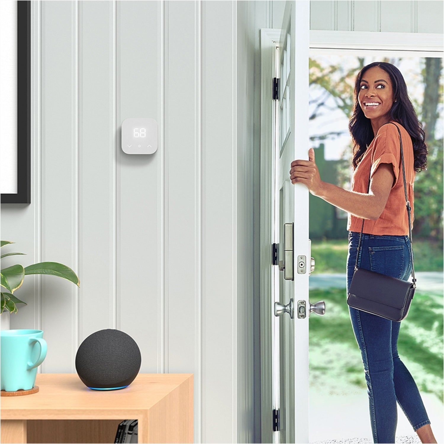 Amazon Smart Thermostat - Woman exiting home, smiles over her shoulder, with Amazon Smart Thermostat on wall and Alexa-enabled device nearby.