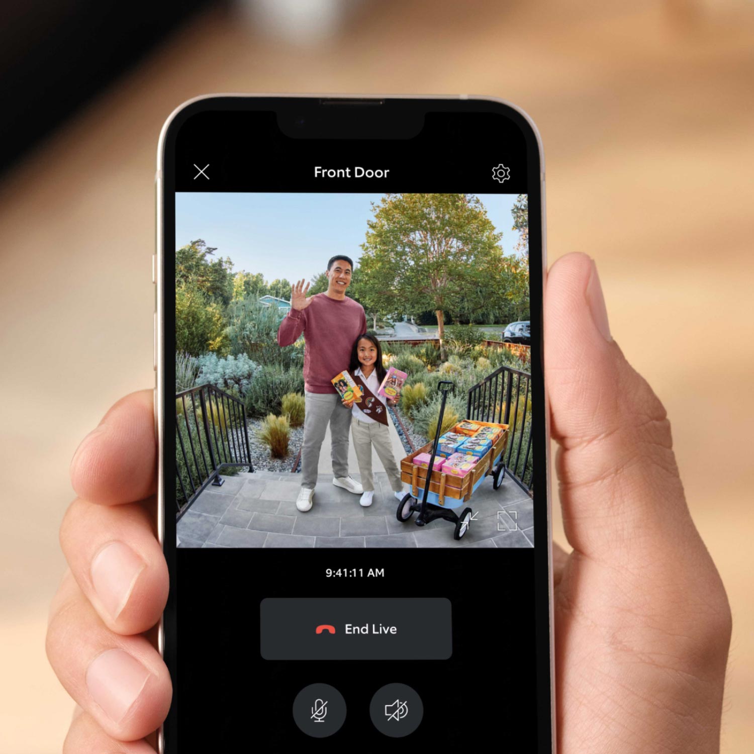 Battery Doorbell Plus - Hand holding a smartphone showing a live Ring video feed of a waving man and child on a front porch selling cookies.