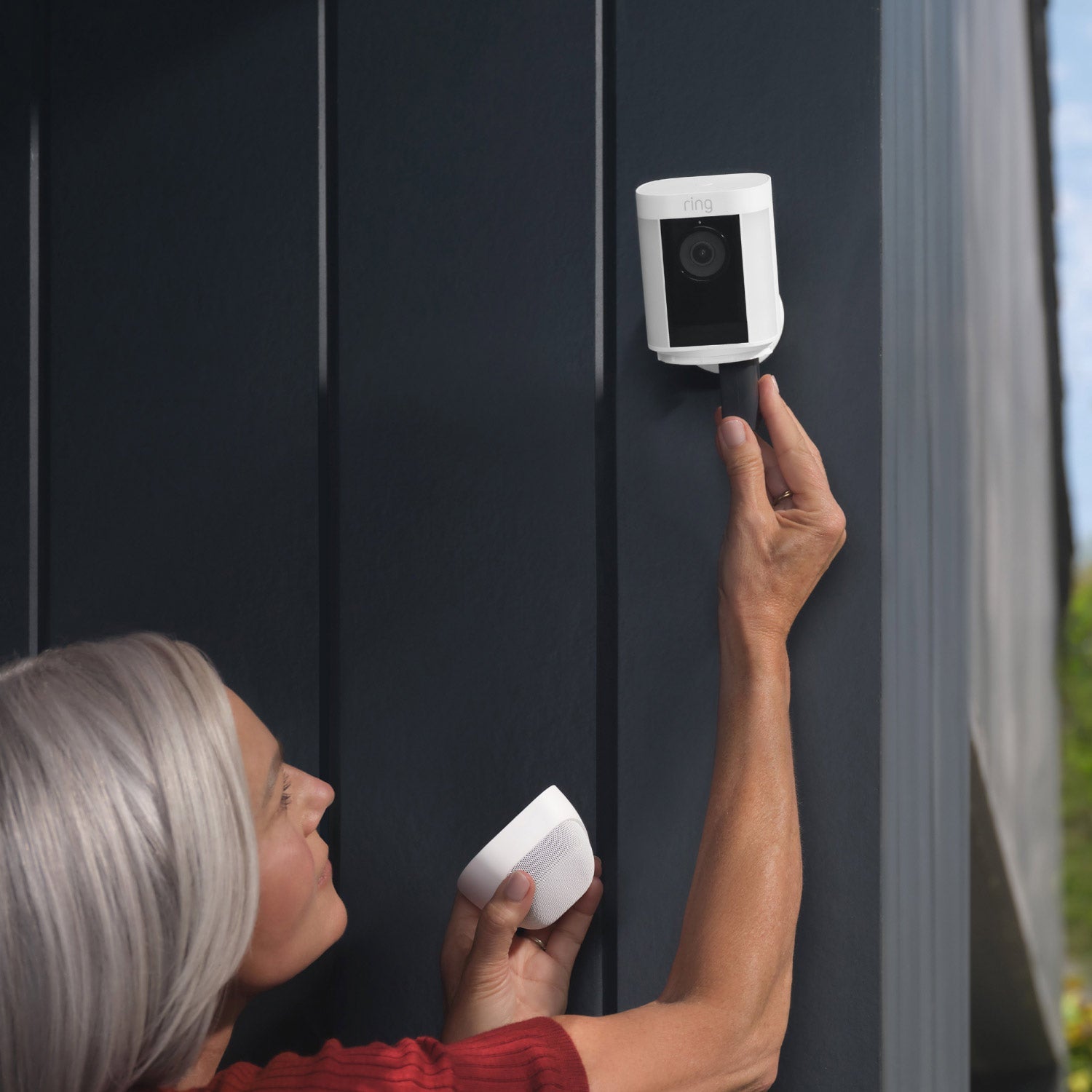 Spotlight Cam Pro (Featuring Retinal 2K) - Battery:Woman inserting a battery into a Spotlight Cam Pro mounted on an outside corner wall of a house.