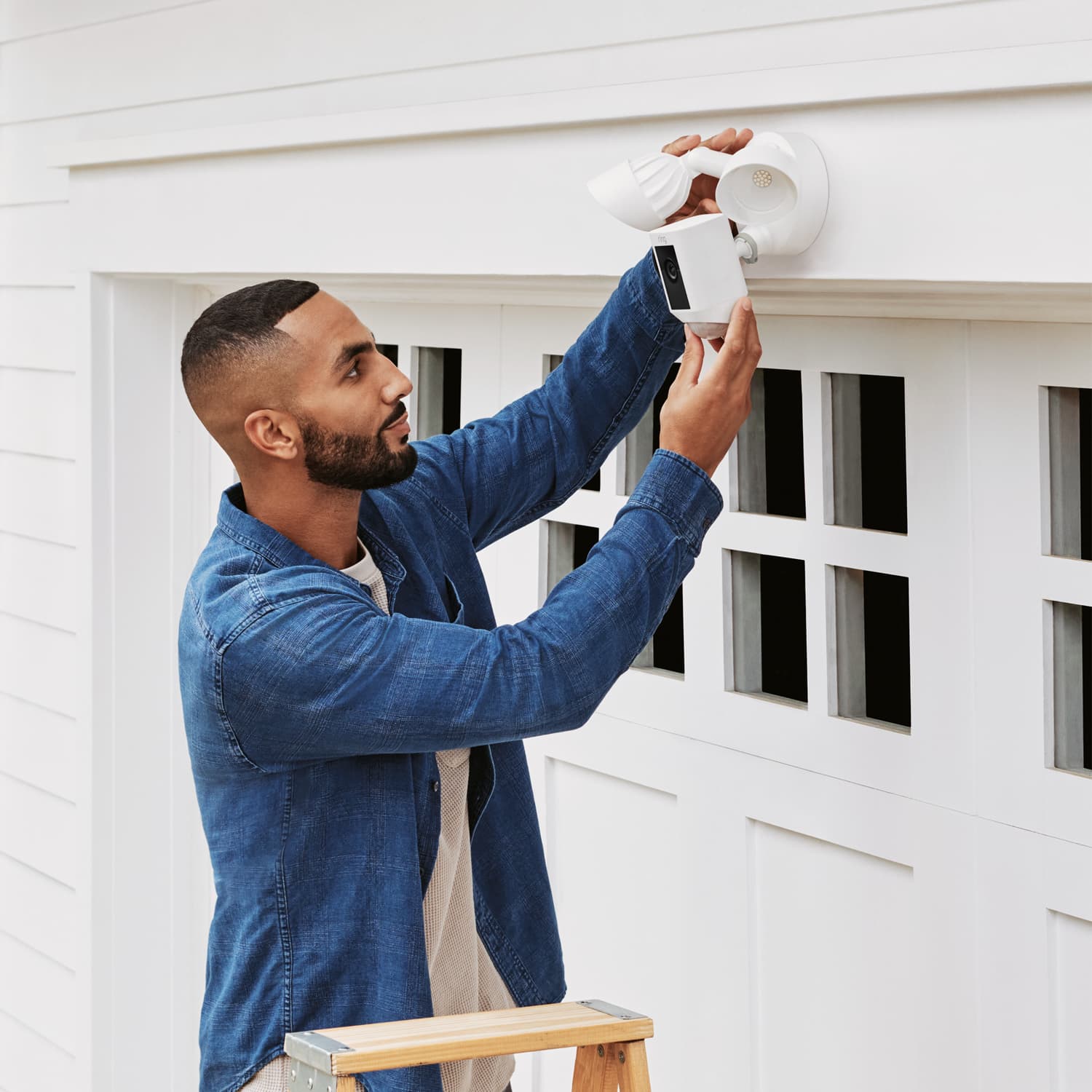Floodlight Cam Plus - Man adjusting the angle of camera and lights on Ring Floodlight Cam Wired Plus mounted over a garage door.