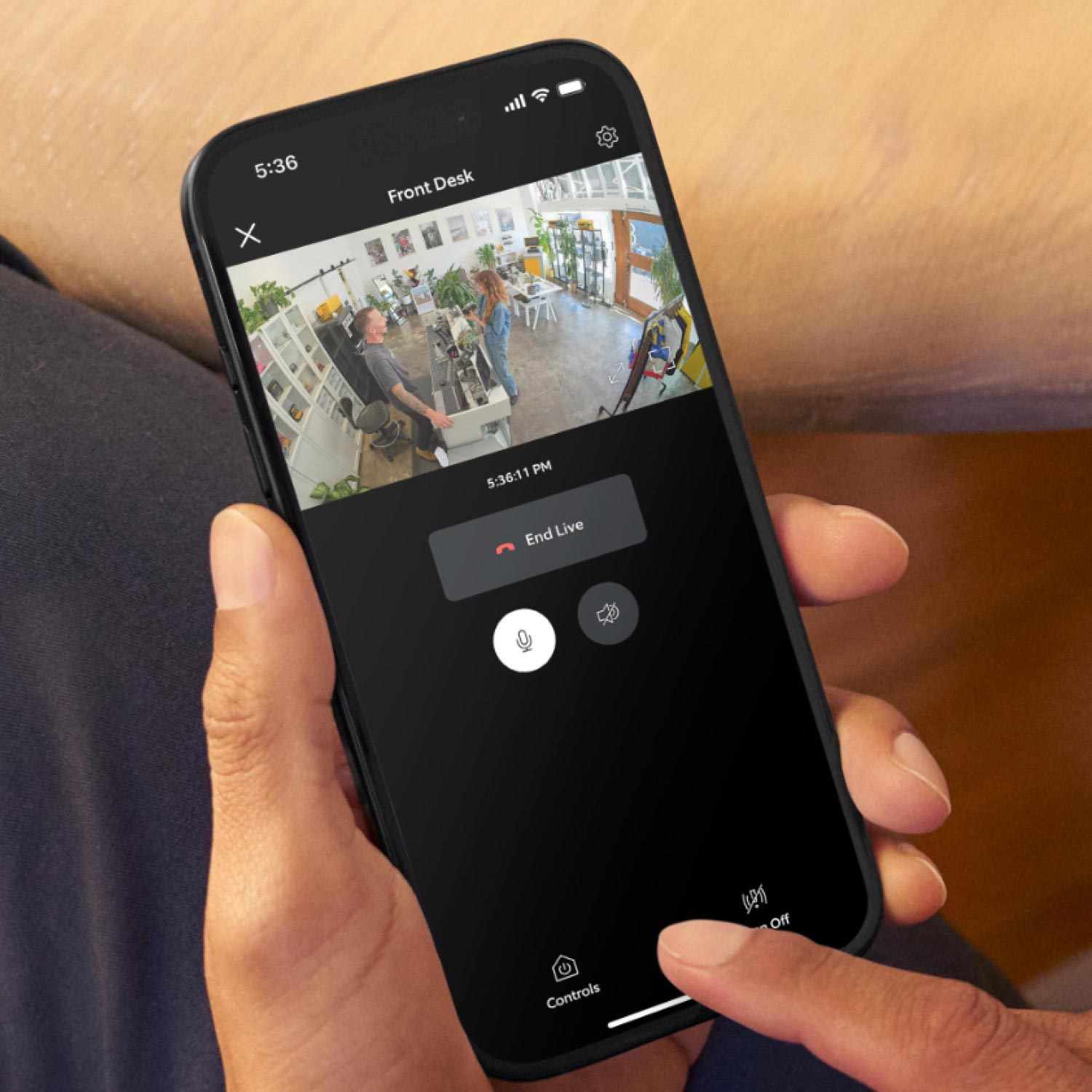 Retail Starter Kit (Plug-In) (Outdoor Cam Plus Plug-In + Pan-Tilt Indoor Cam) - Hand holding a phone with the Ring App on the screen. There is security footage of a customer being served at a checkout desk.