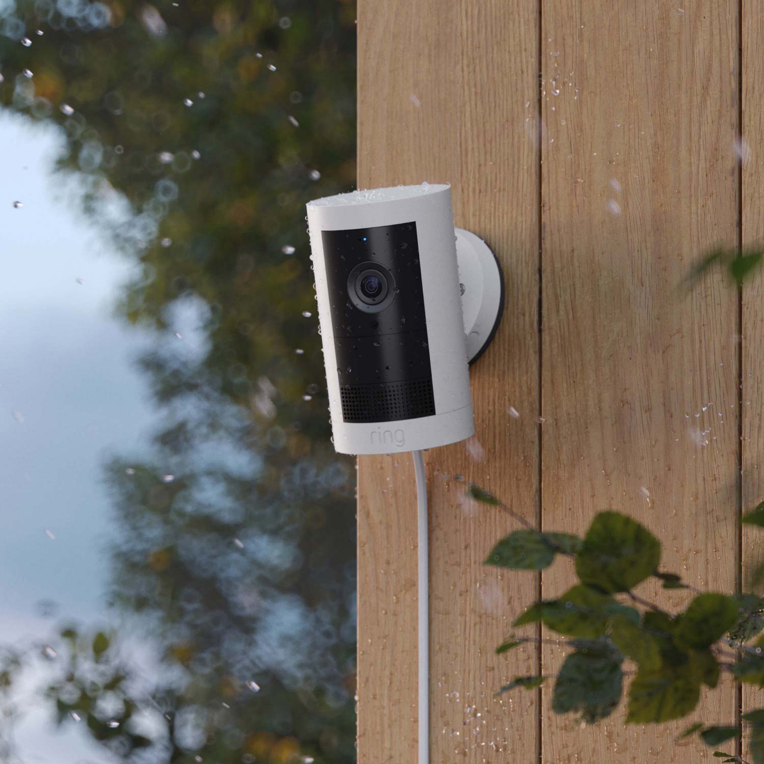 Outdoor Cam Plus (Featuring Retinal 2K)  - Plug-In:White Ring Outdoor Cam Plus mounted on wood wall, covered in raindrops, with rain falling.