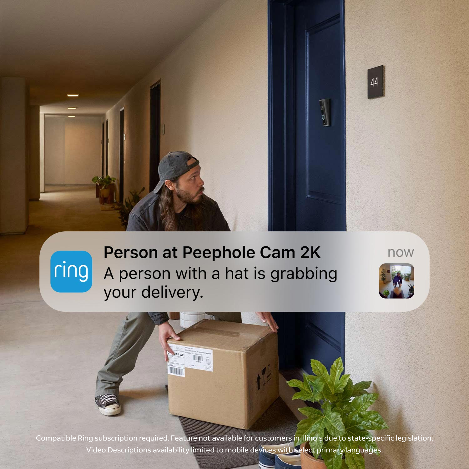 Peephole Cam 2K - Hallway scene: person in a cap crouches to lift a large delivery box at a blue apartment door with a doorbell camera.