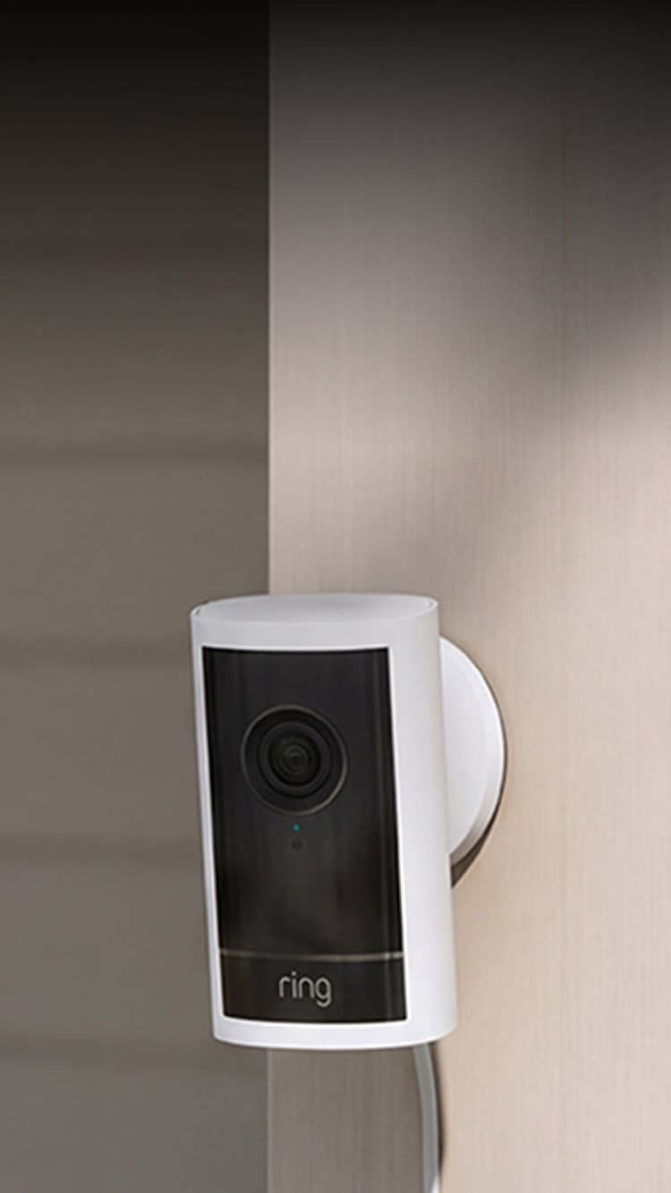White Ring security camera mounted on an exterior wall near a window, with a power cable running down.