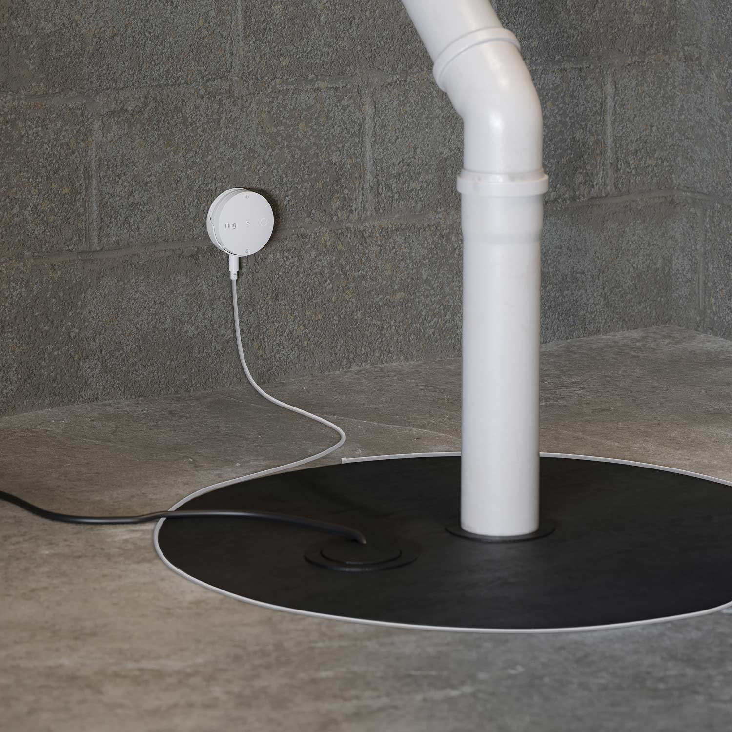 Sump Pump Monitor (Ring Sensors) - Ring alarm sensor mounted on concrete wall next to white PVC pipe, with wire running through floor opening.