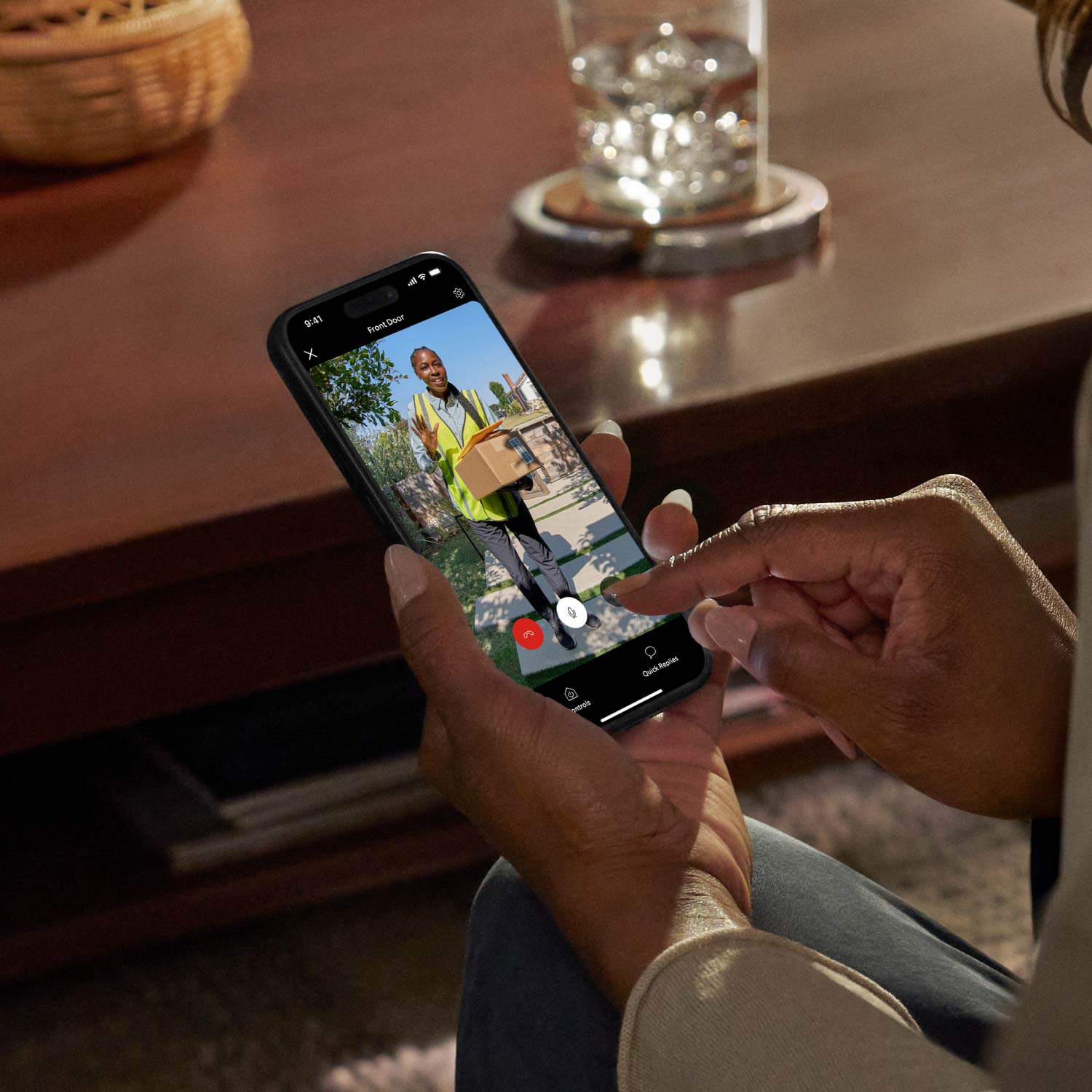 Wired Doorbell Elite (Newest Model) - Person using phone at a wooden table. There is a delivery worker on screen with a package.