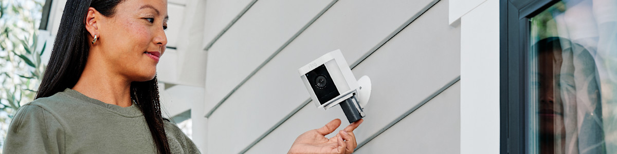 Person inserting a quick release battery into a white Ring security camera on a wall. 