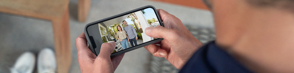 Hands holding a smartphone displaying a couple in front of a house