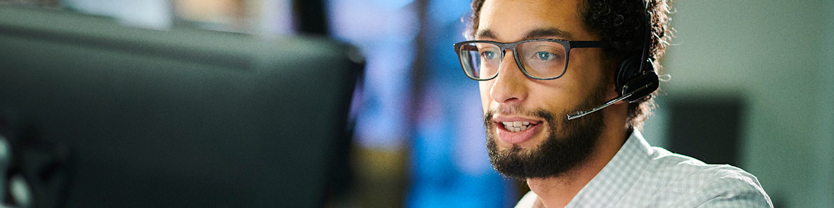 Professional wearing glasses smiles while working at computer monitors