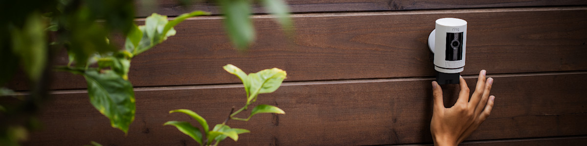 Hand installing a Ring Quick Release battery in a Ring security camera on a wooden fence