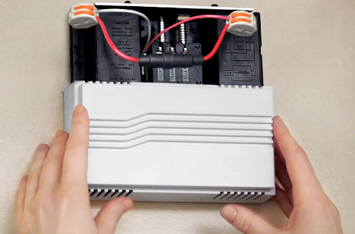 An existing doorbell with a Pro Power Kit installed and hands replacing the cover. 